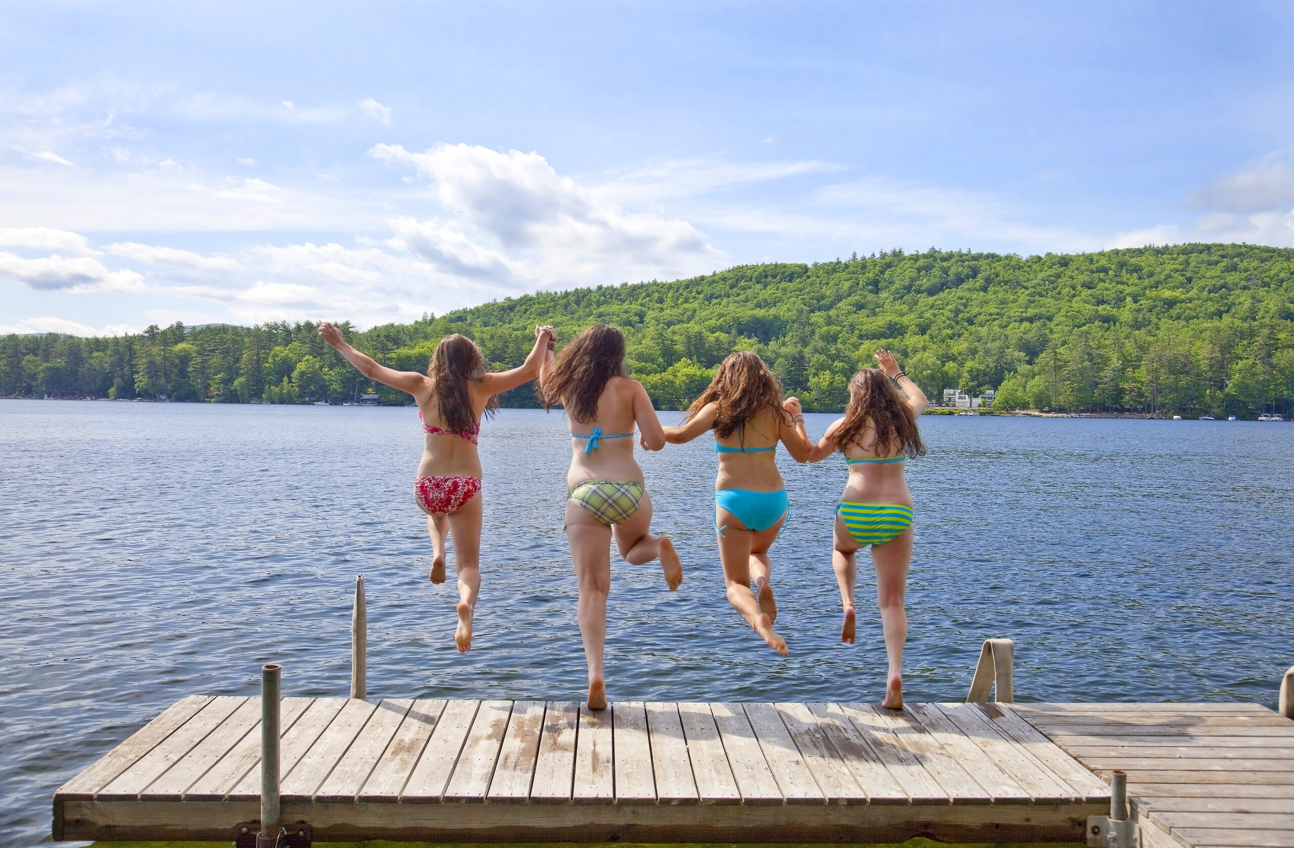 Four Girls Jumping Off A Dock At A Lake